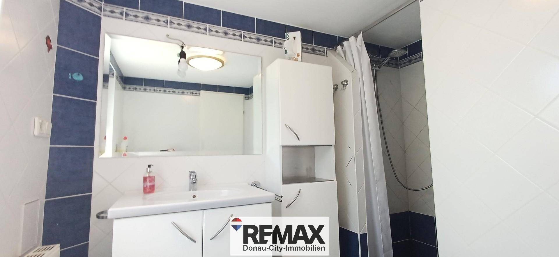 Badezimmer mit Waschbecken, Spiegelschrank, Duschbereich und blauen Akzentfliesen.