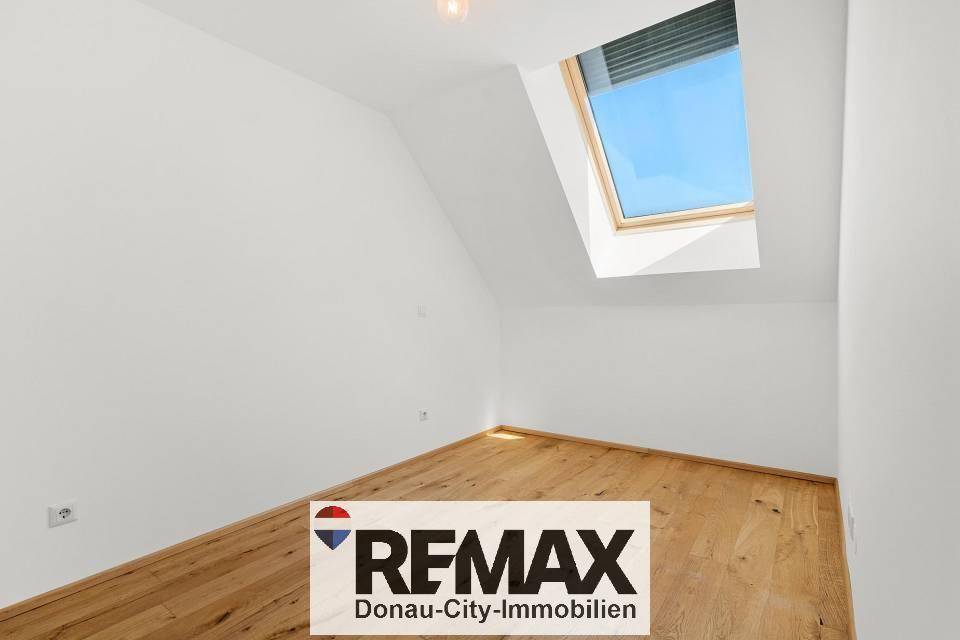 Helles Zimmer mit Holzboden und einem Dachfenster, das mit einem Rollo ausgestattet ist.