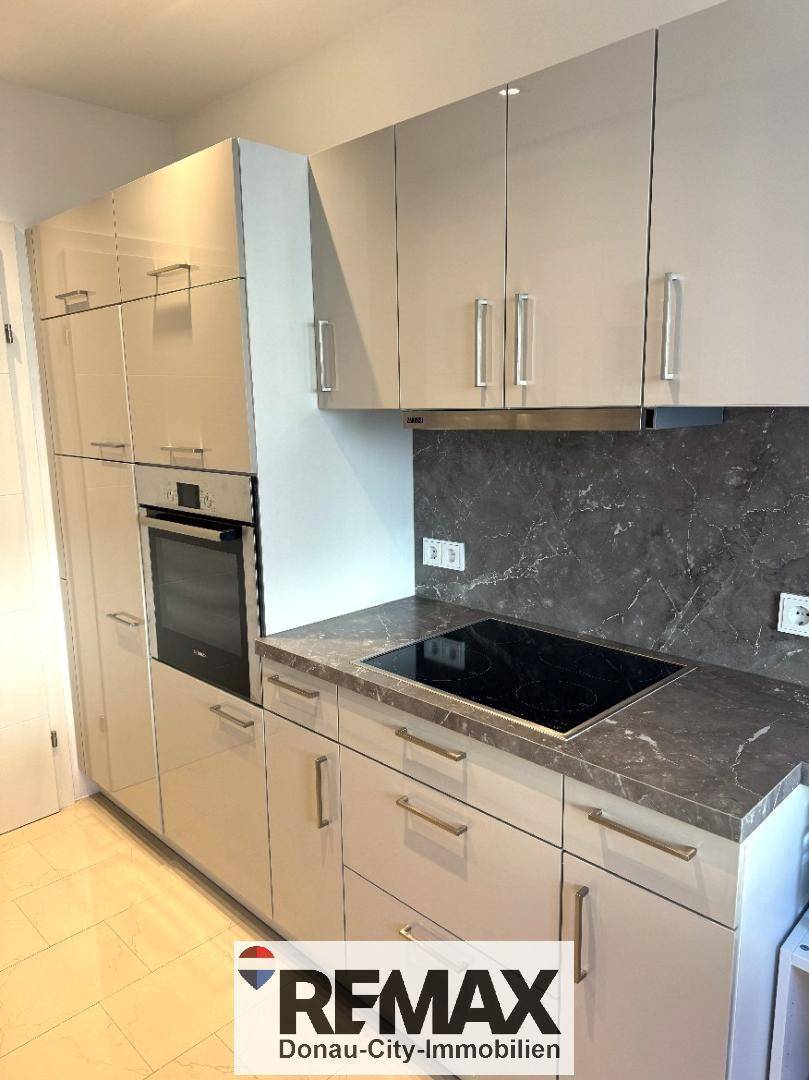 Einbauküche mit integriertem Backofen, Induktionskochfeld und glänzenden Oberschränken.