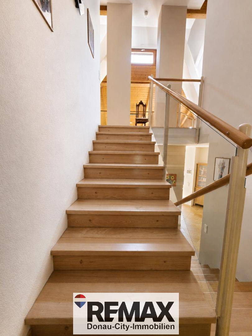 Elegante Holztreppe mit Glasgeländer führt in die oberen Etagen, hell und offen gestaltet.