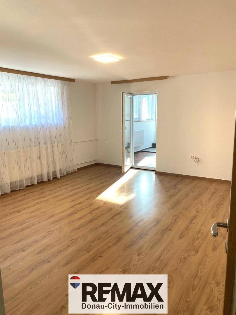 Geräumiger Raum mit Laminatboden und Zugang zu einem weiteren hellen Zimmer.