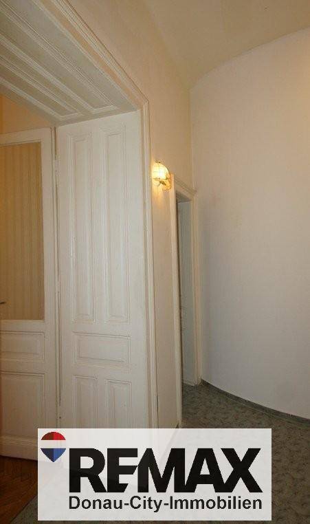 Heller Flur mit Teppichboden und einer Wandleuchte, die den Eingangsbereich beleuchtet.