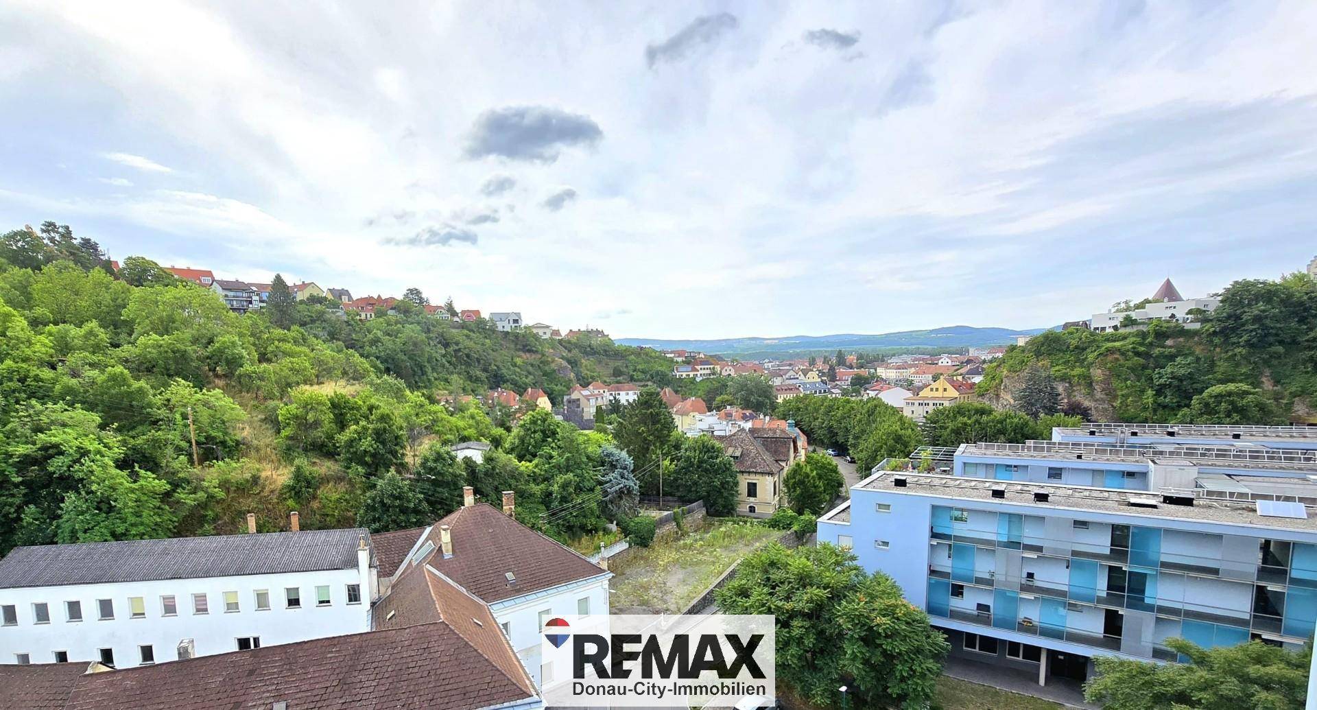 Weitläufiger Blick über die Stadt und die umliegende Landschaft mit bewaldeten Hügeln.