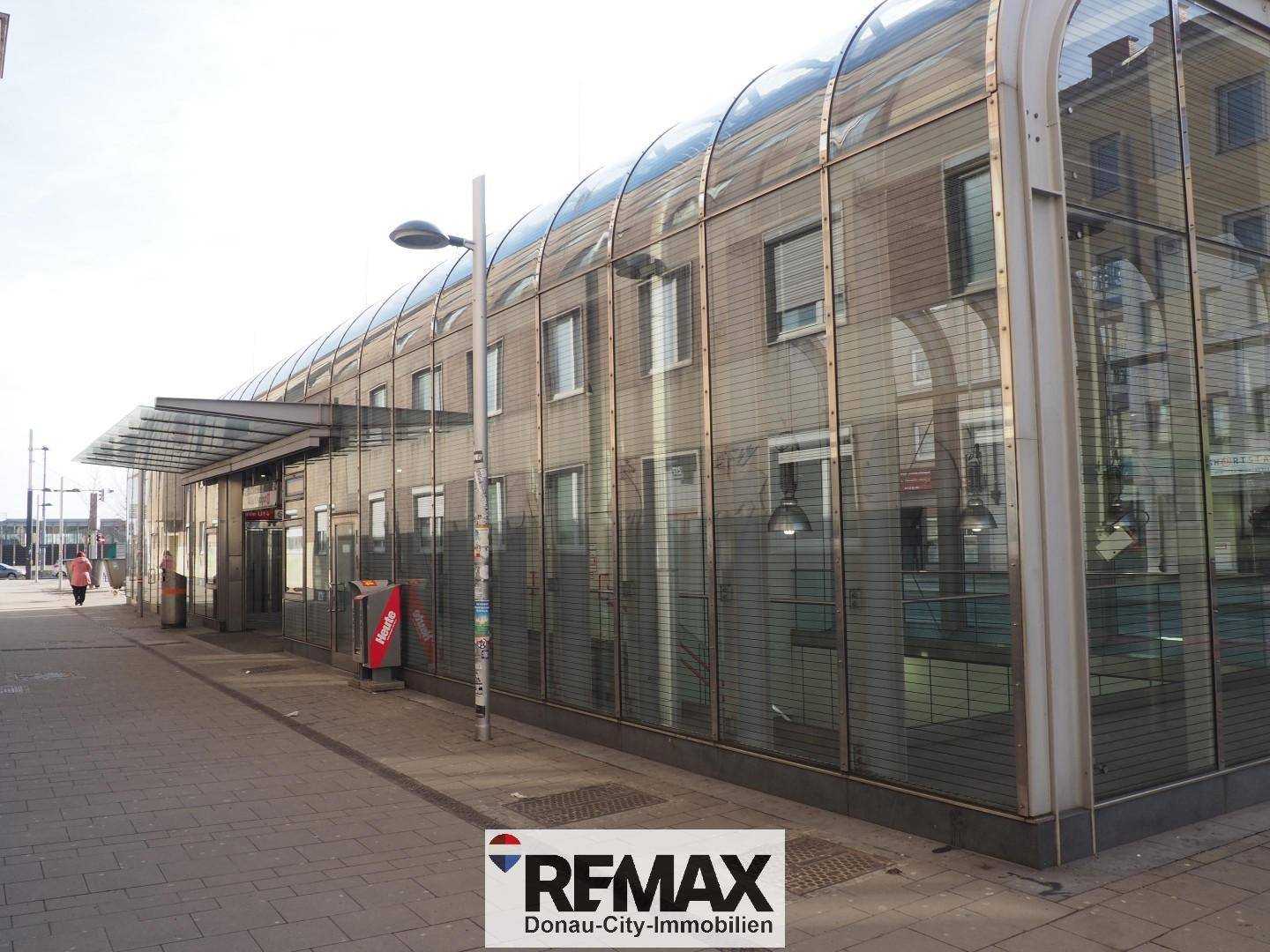 Moderne Glasfassade eines Gebäudes mit gewölbtem Dach und Gehweg davor, möglicherweise ein Geschäftshaus.