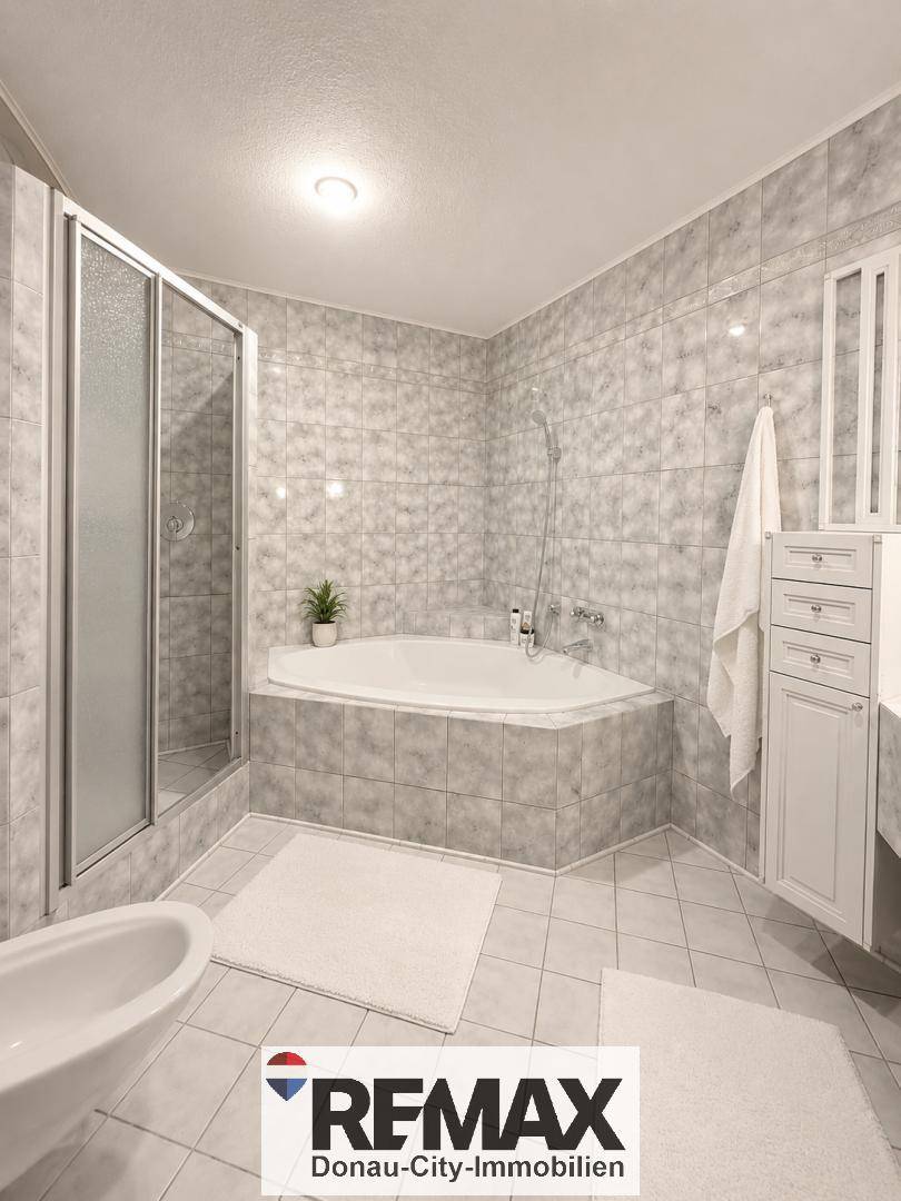 Modernes Badezimmer mit Eckbadewanne, Duschkabine und hellgrauen Fliesen.
