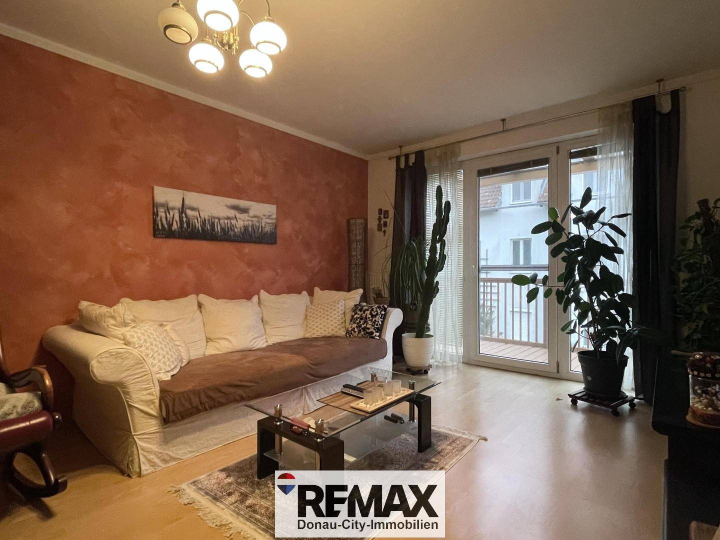 Gemütliches Wohnzimmer mit Sofa, Holzboden und Zugang zu einem Balkon.