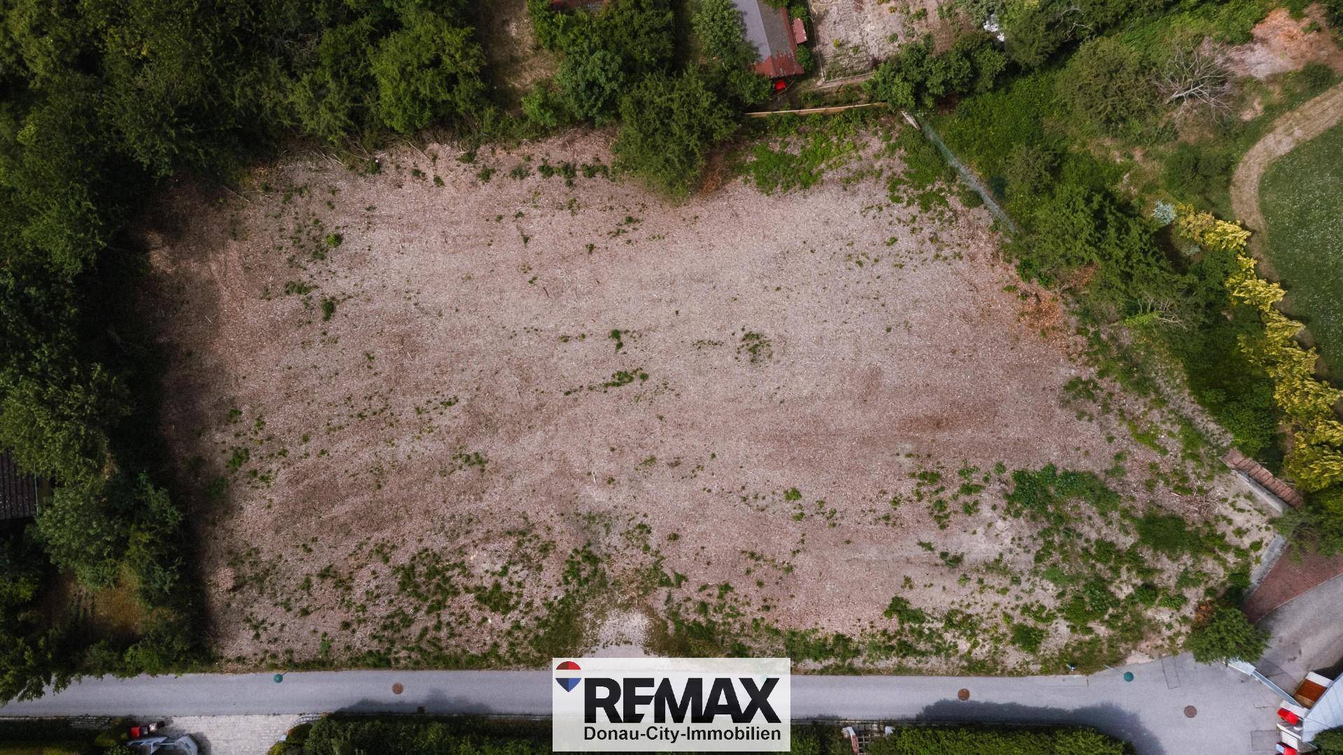 Luftaufnahme eines unbebauten Grundstücks mit leichter Vegetation und angrenzender Straße.