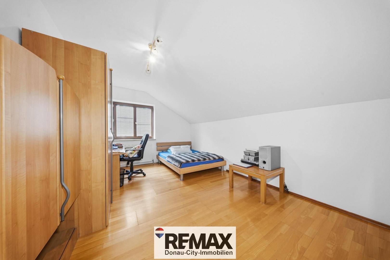 Schlafzimmer im Dachgeschoss mit Holzbett, Schreibtisch und Laminatboden, unter der Dachschräge.