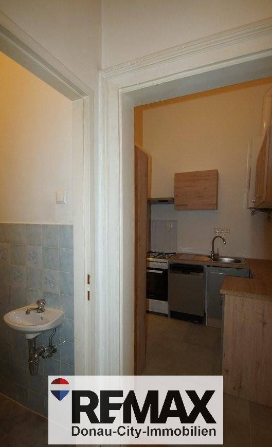 Blick von der Toilette in die kleine Küche mit Holzoptik-Arbeitsplatte und Spüle.