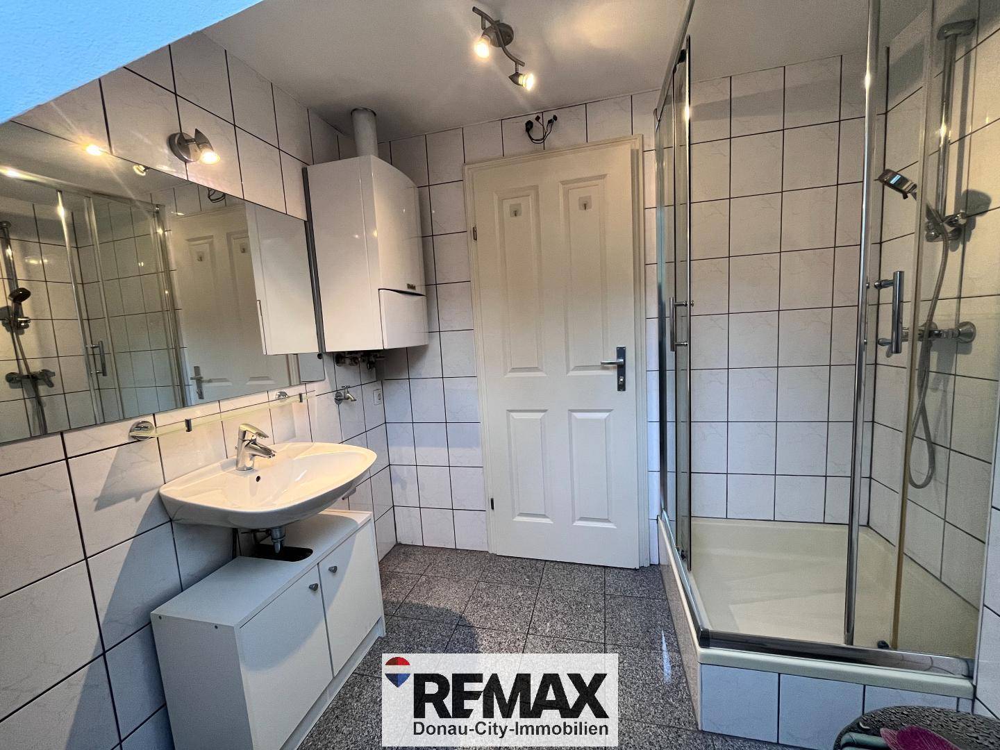 Gefliestes Badezimmer mit Duschkabine, Waschbecken und Spiegelschrank.