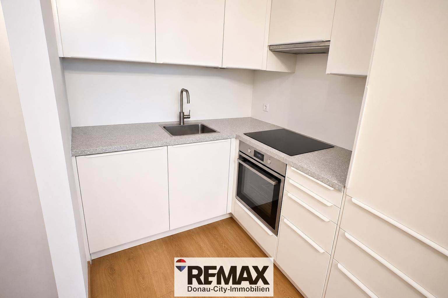Moderne Einbauküche mit weißen Schränken, Spüle, Induktionskochfeld und integriertem Backofen.