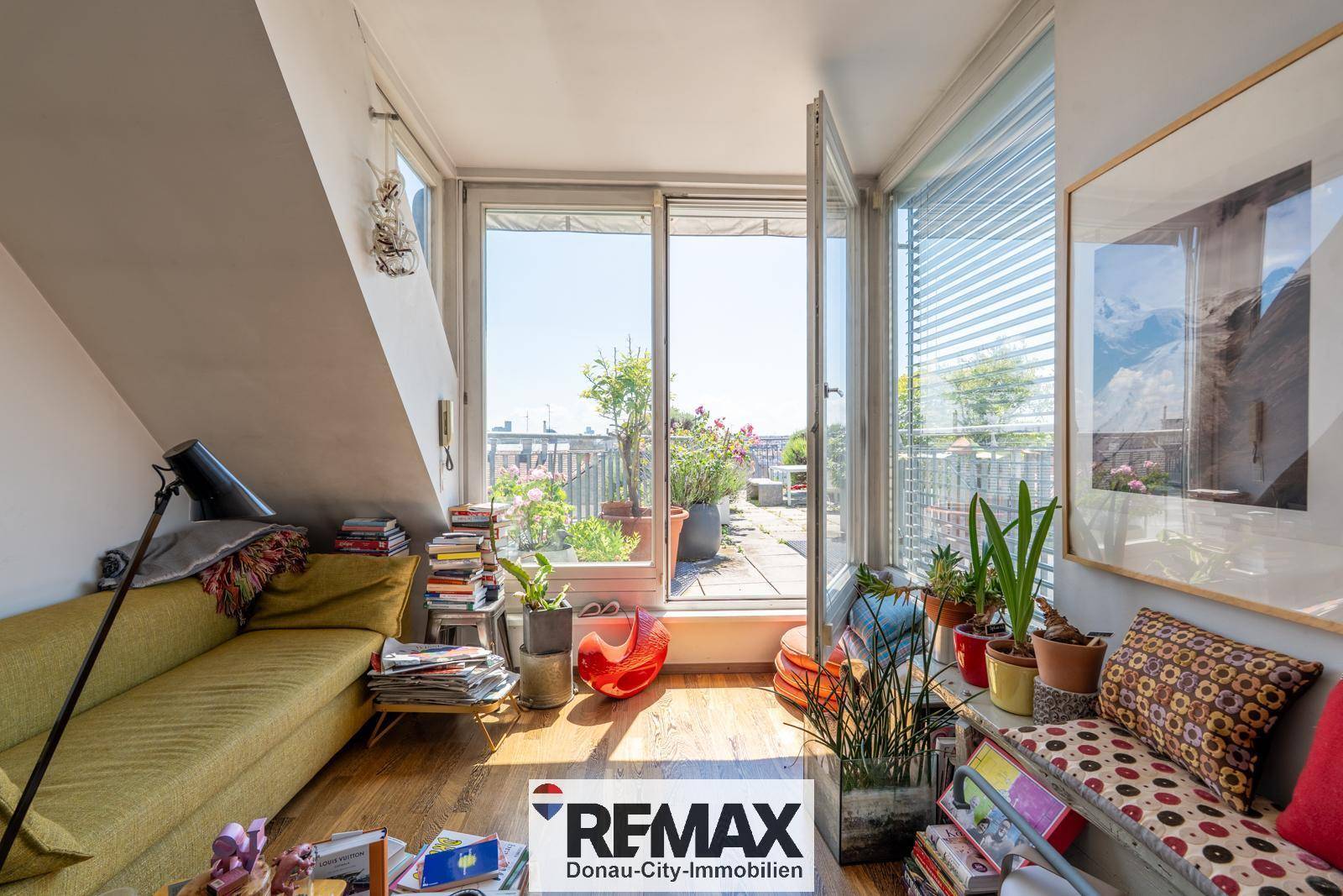 Wohnzimmer mit Holzboden und großen Glasfenstern, die Zugang zu einer sonnigen Dachterrasse bieten.