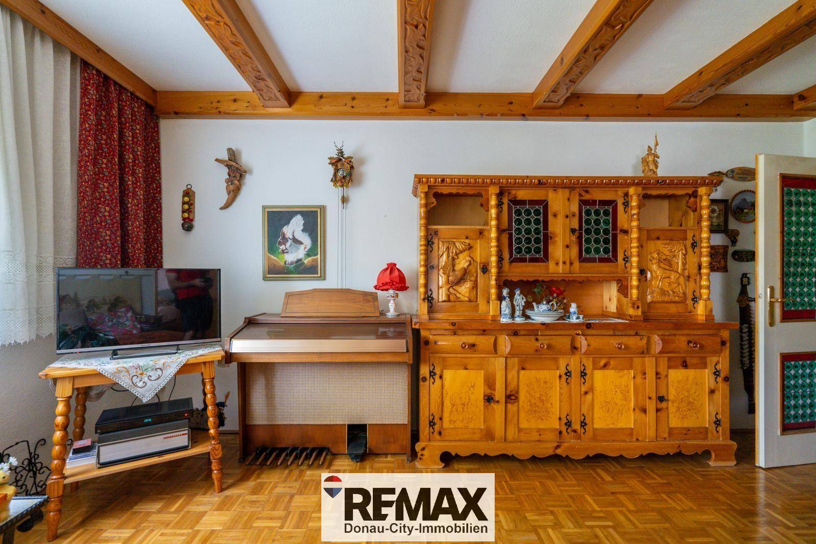 Wohnbereich mit Holzbalkendecke, traditionellem Sideboard und Klavier.