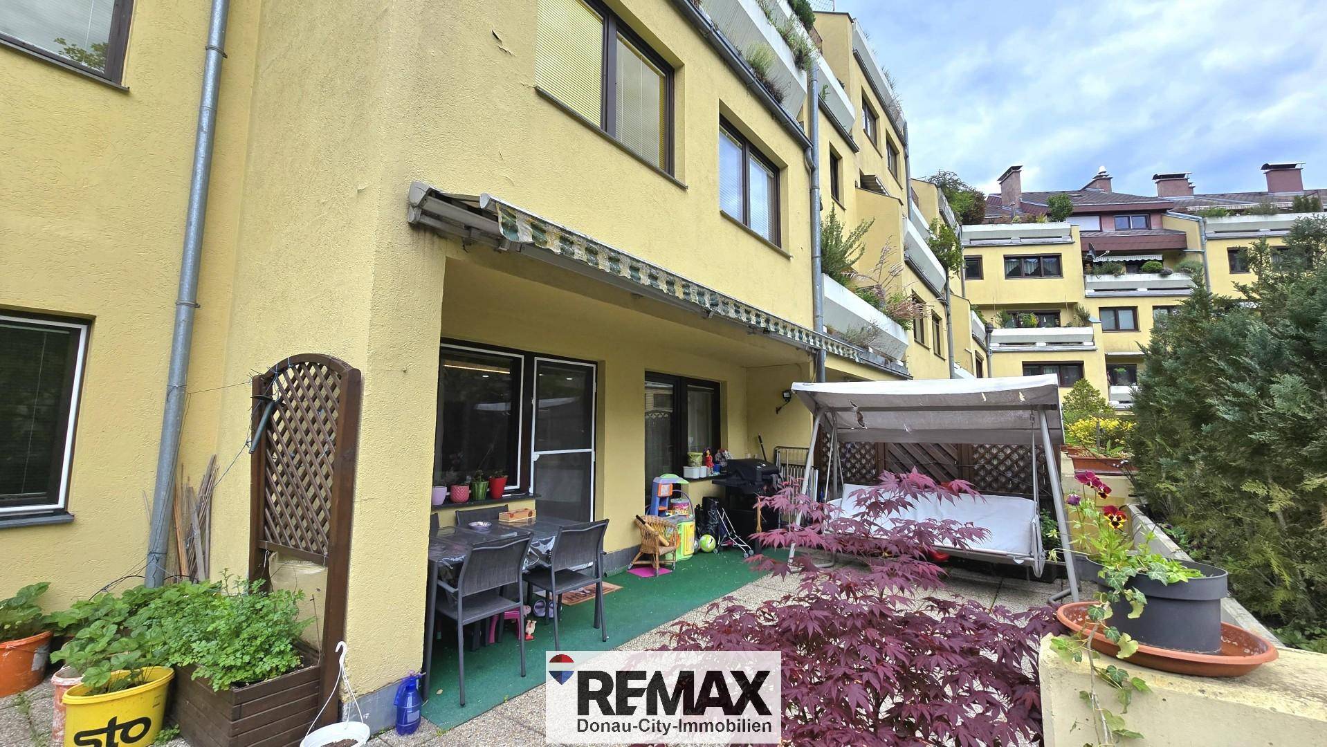 Erdgeschoss-Terrasse mit Sitzgelegenheiten, Pflanzen und Blick auf die Gebäudefassade.