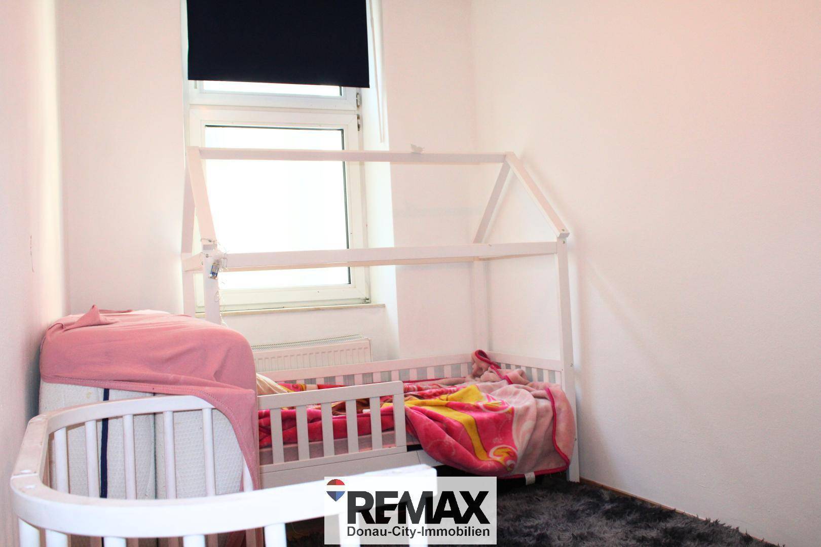 Kinderzimmer mit zwei Kinderbetten, einem Fenster und einem flauschigen Teppichboden.