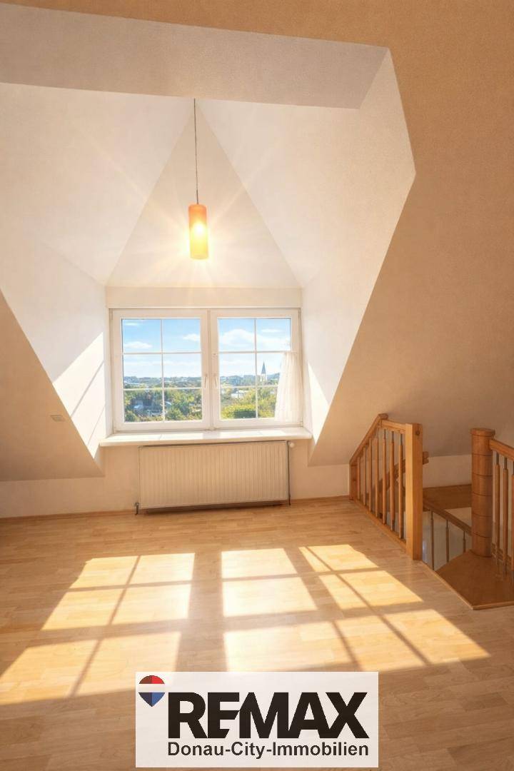 Heller Dachraum mit großen Fenstern, Heizkörper und Holzfußboden, mit Treppenzugang.