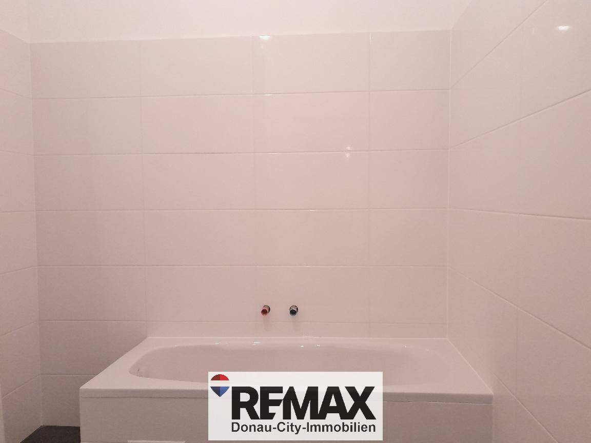 Modernes Badezimmer mit weißer Badewanne und großen weißen Fliesen an den Wänden.
