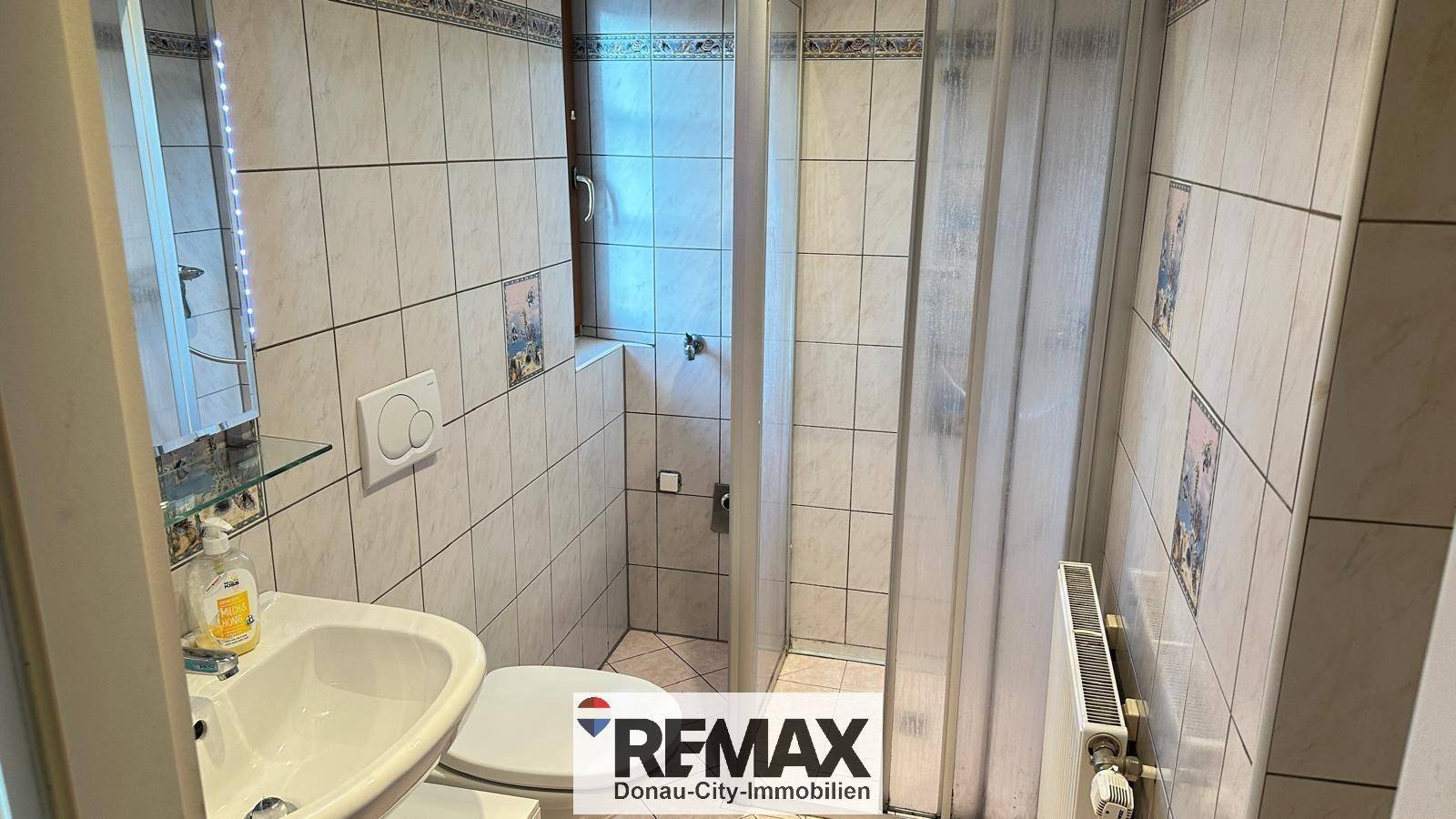 Gefliestes Badezimmer mit Dusche, WC, Waschbecken und einem Fenster für Tageslicht.
