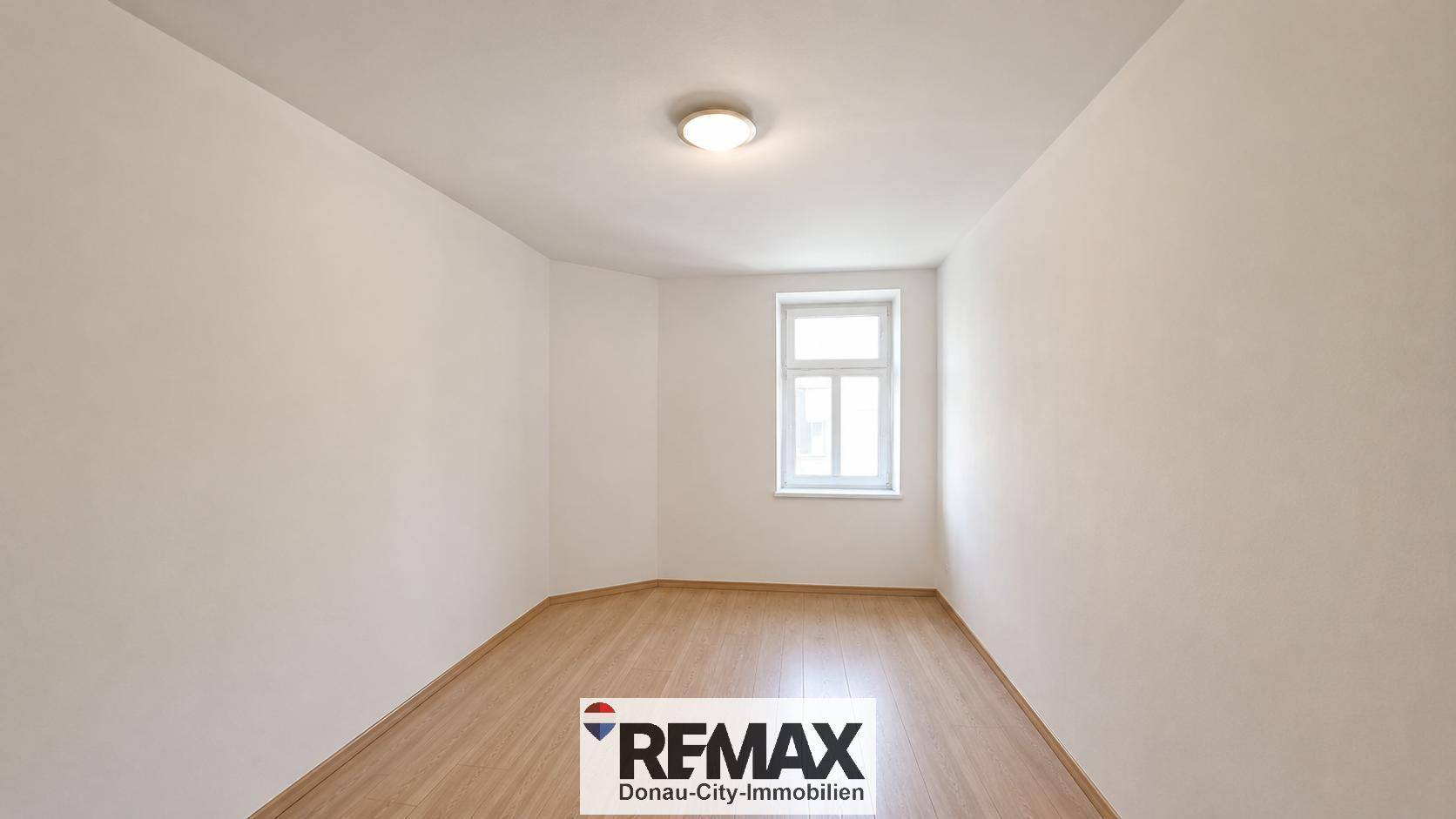 Helles, leeres Zimmer mit Holzfußboden und einem Fenster, das viel natürliches Licht bietet.
