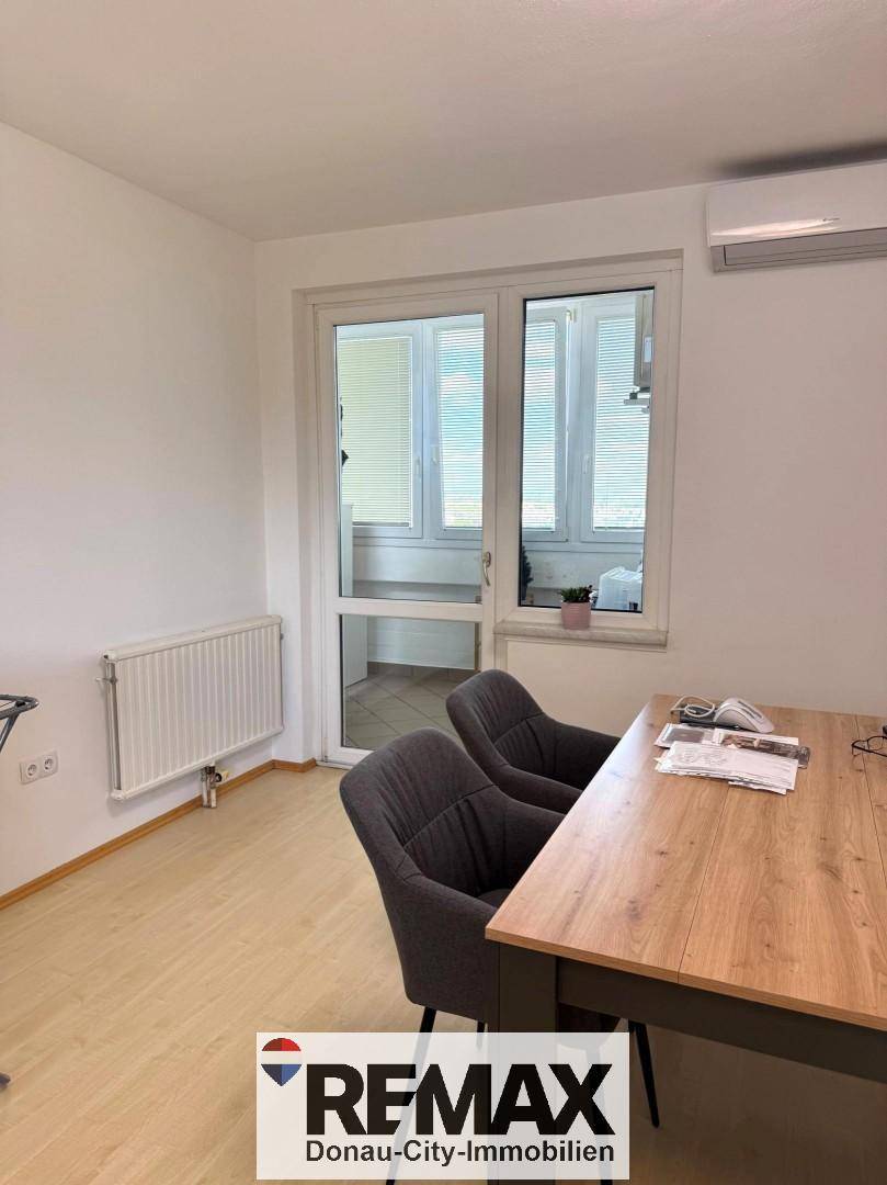 Heller Raum mit Holztisch, Stühlen und Zugang zu einem verglasten Balkon.