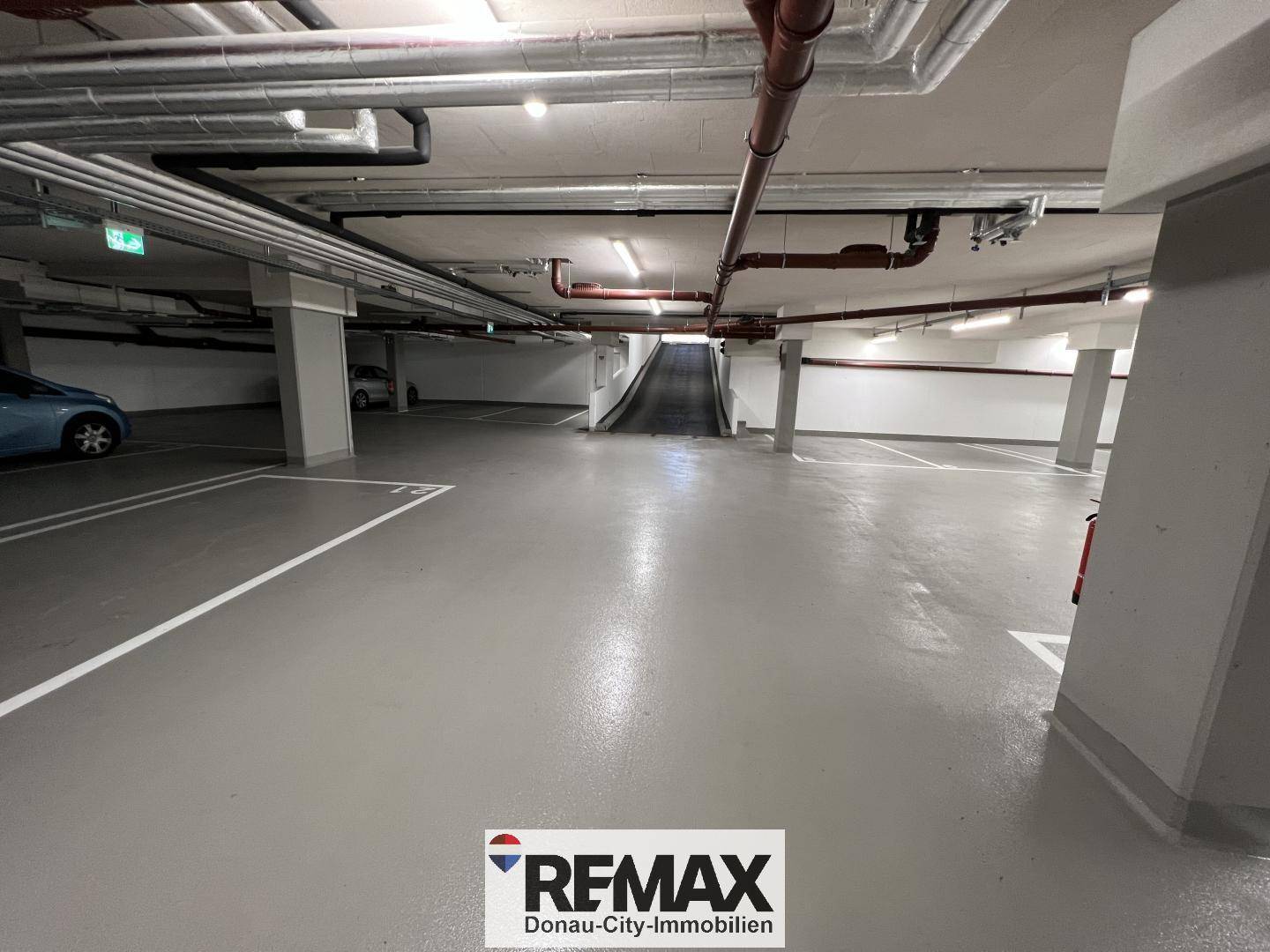 Geräumige Tiefgarage mit markierten Parkplätzen und sichtbaren Installationen an der Decke.