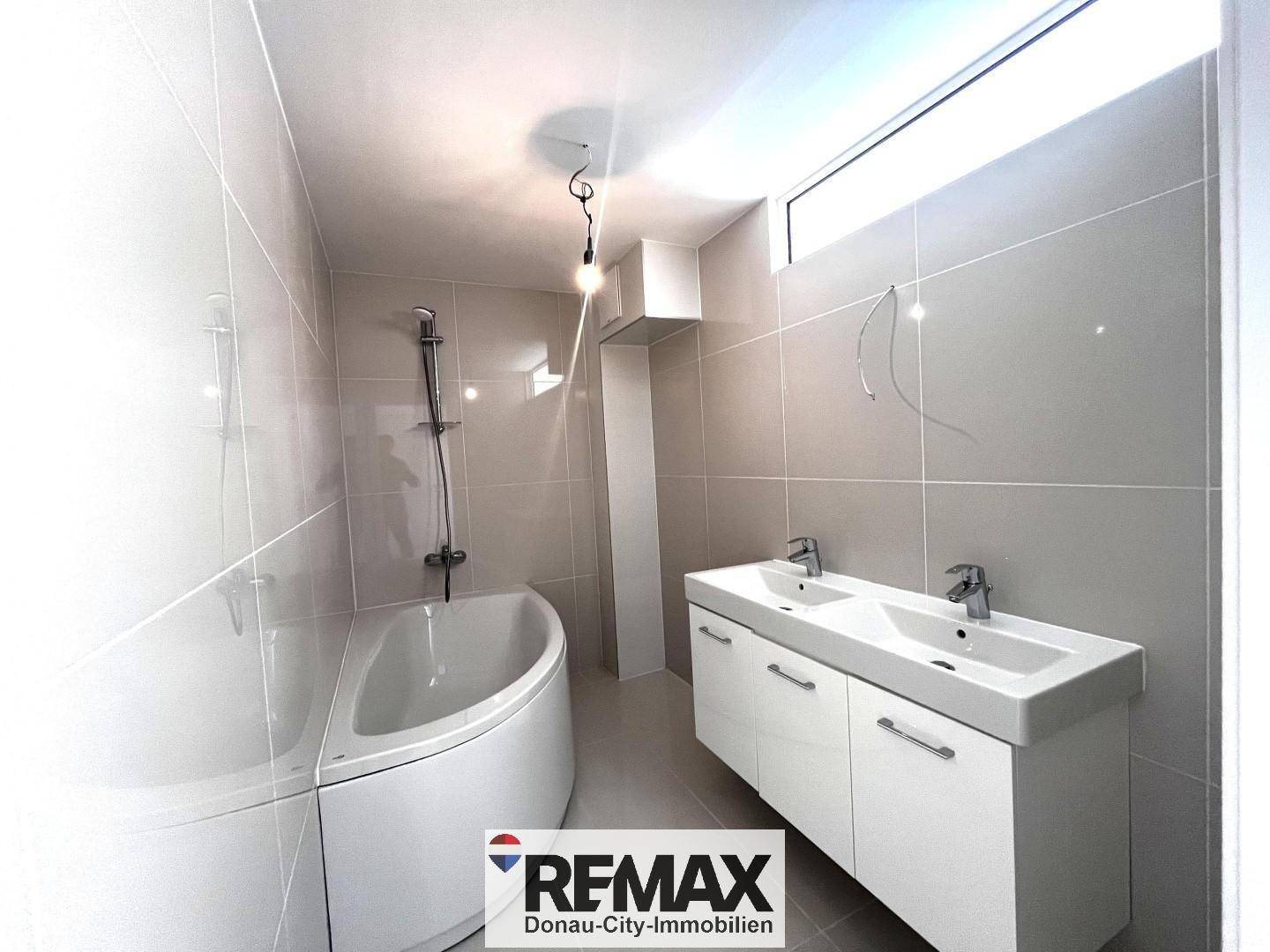 Modernes Badezimmer mit Eckbadewanne, Doppelwaschbecken und hellen Fliesen.