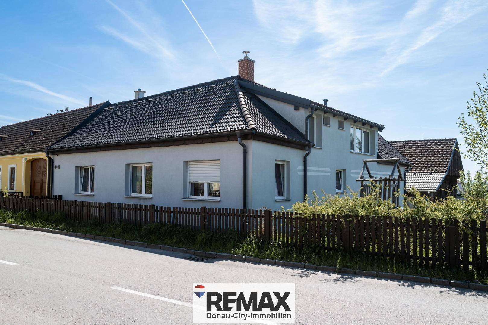 Ansicht des Hauses von der Straße mit Zaun und gepflegter Fassade unter blauem Himmel.