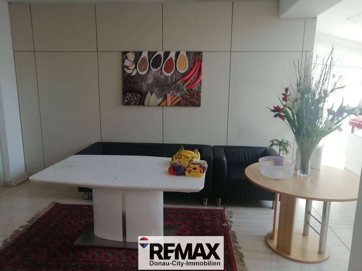 Gemütlicher Wartebereich mit schwarzem Ledersofa, Teppich und dekorativen Elementen in einem Büro.