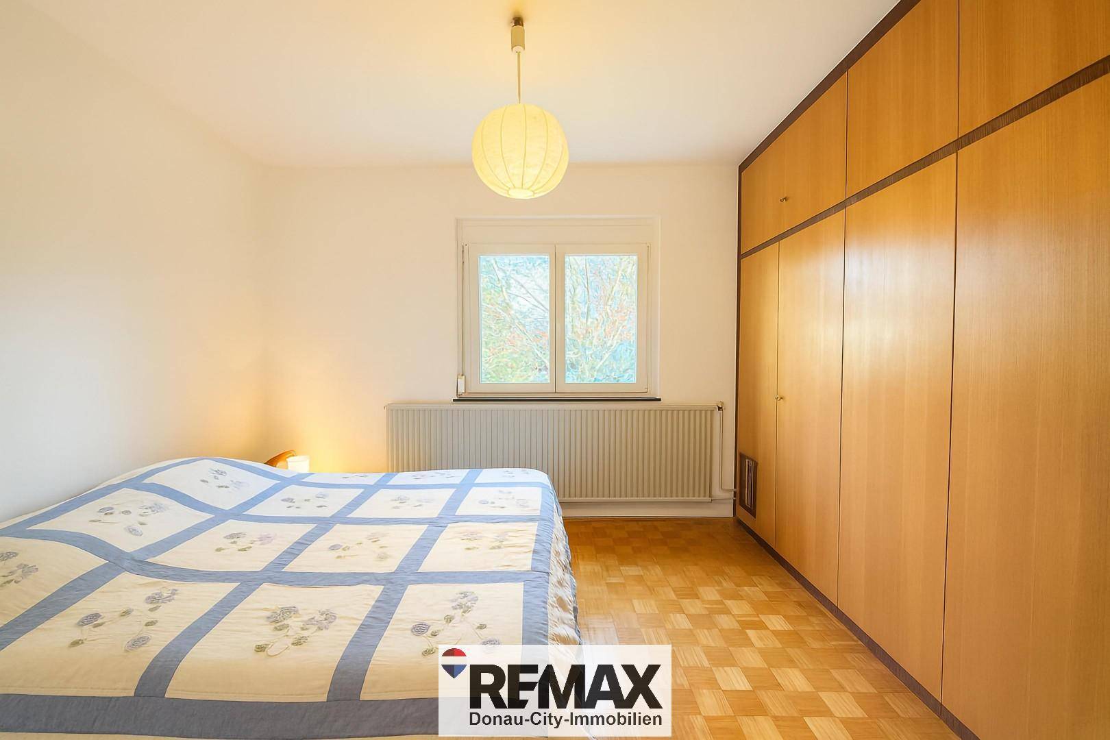 Schlafzimmer mit Parkettboden, großem Fenster und geräumigem Kleiderschrank.