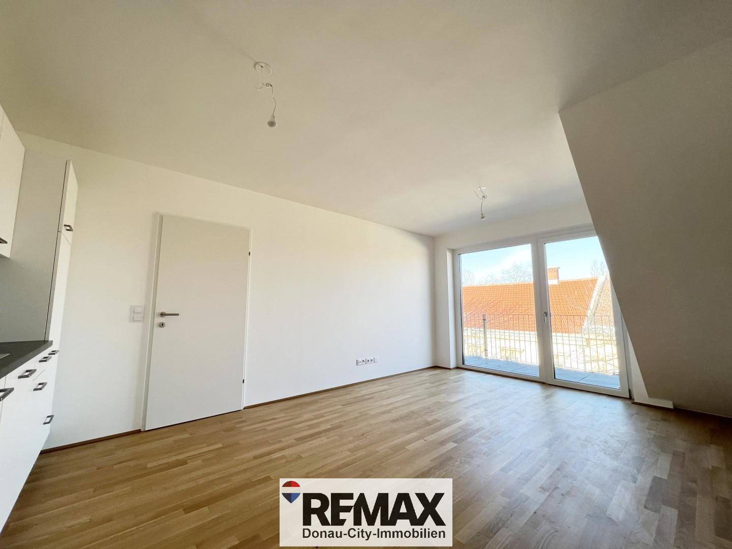 Geräumiger, leerer Wohnbereich mit Holzboden, großen Fenstern und Zugang zum Balkon.