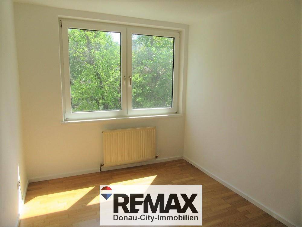 Gemütliches Schlafzimmer mit Parkettboden, Fenster und Blick auf Bäume.