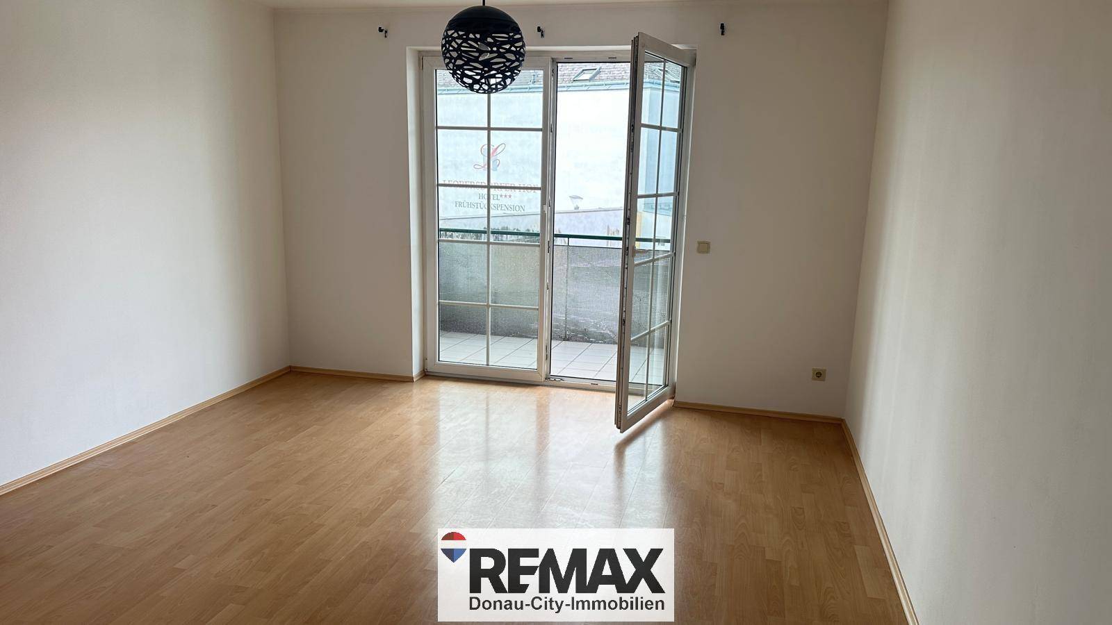 Heller Raum mit Parkettboden und Zugang zu einem Balkon durch eine große Glastür.