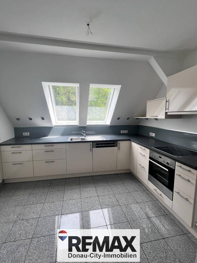 Moderne Küche mit hellen Einbauschränken, dunkler Arbeitsplatte und Dachfenstern.