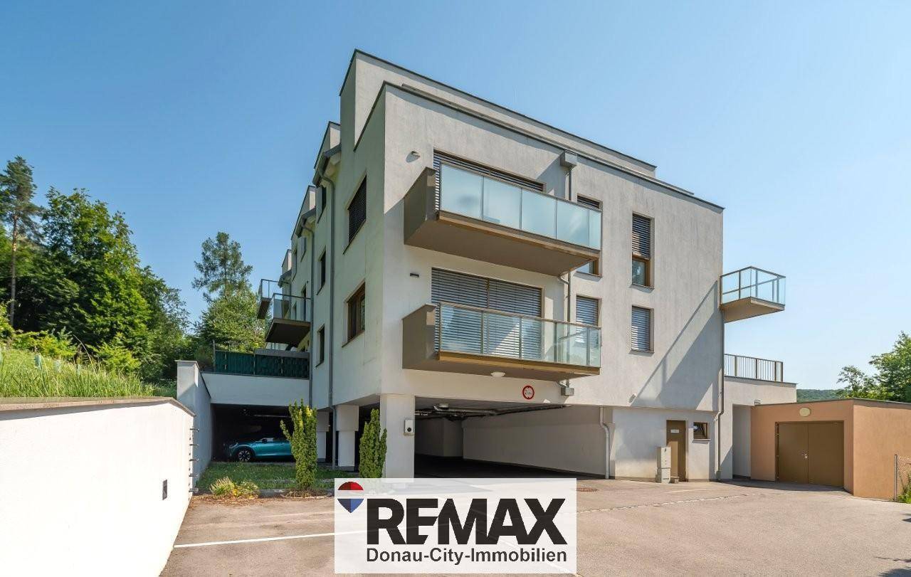 Modernes Mehrfamilienhaus mit Balkonen und Tiefgaragenzufahrt in grüner Umgebung.