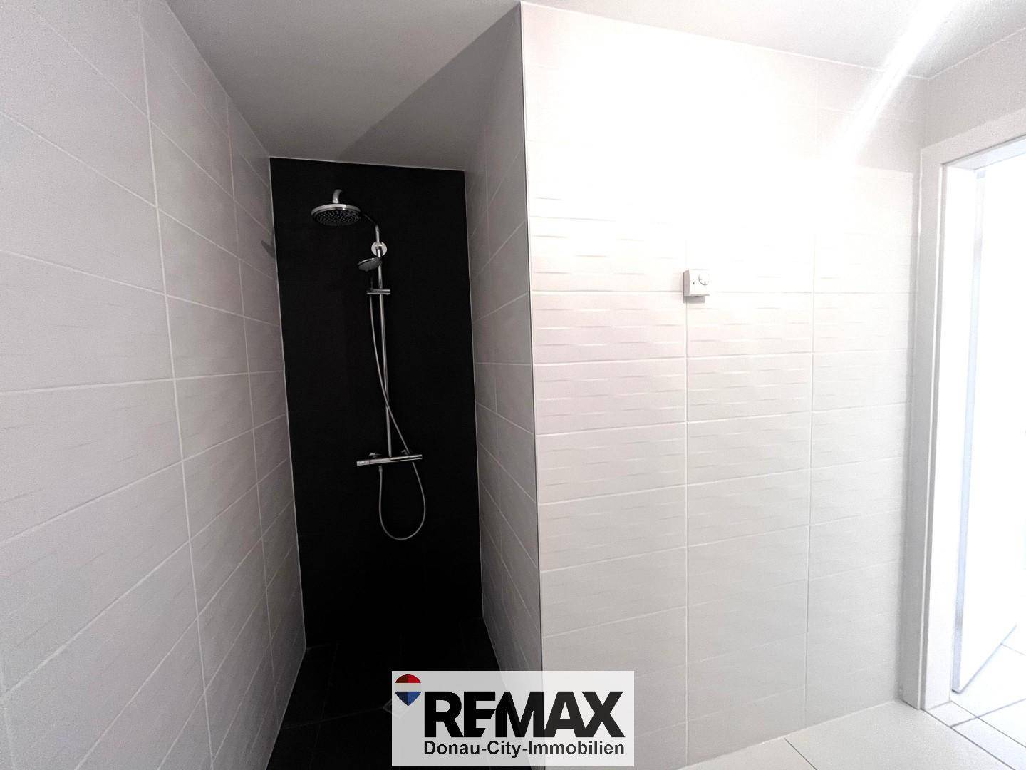 Moderne Duschkabine mit schwarzen Fliesen und einer Regendusche, die ein luxuriöses Gefühl vermittelt.