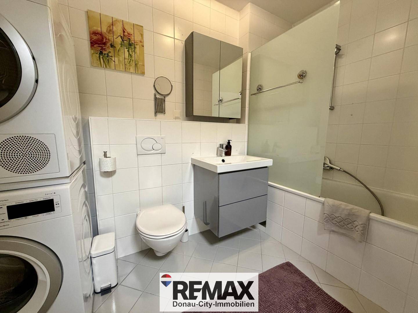 Funktionales Badezimmer mit Badewanne, WC, Waschbecken und Waschmaschine, hell gefliest.
