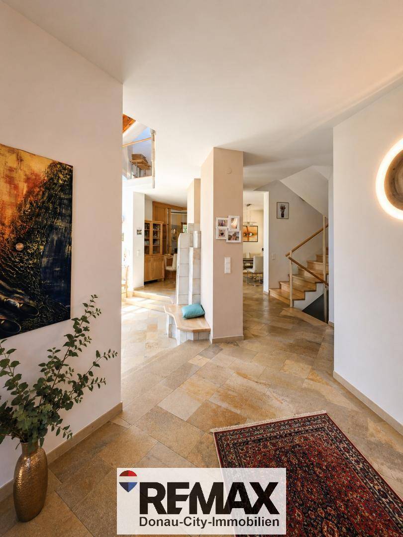 Heller Eingangsbereich mit Natursteinboden, Kunstwerken an den Wänden und Blick auf die Treppe.