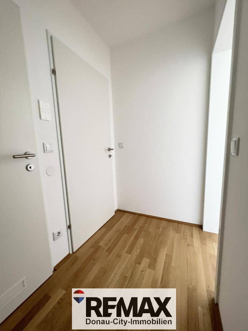 Heller Flur mit Holzboden und weißen Wänden, der zu weiteren Räumen führt.