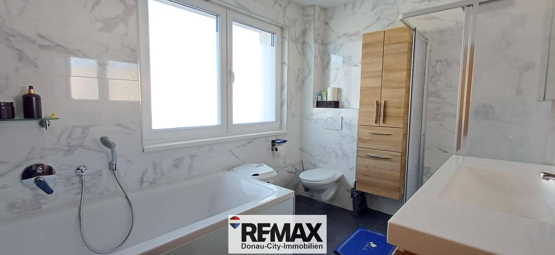 Modernes Badezimmer mit Badewanne, Dusche, Fenster und Marmorfliesen.