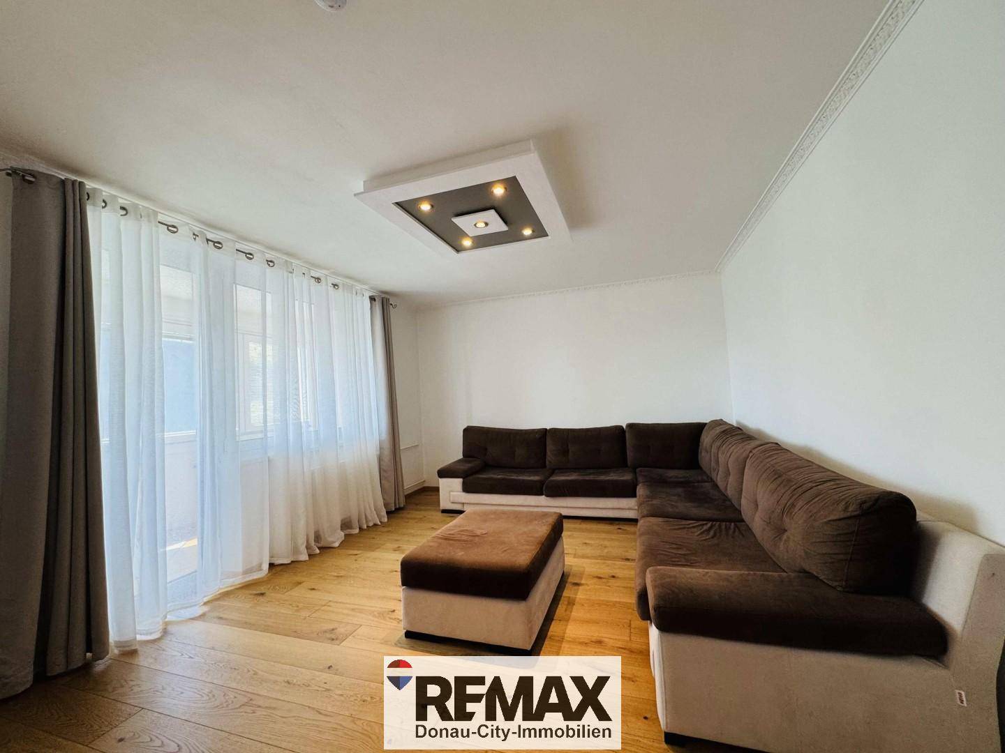 Geräumiges Wohnzimmer mit großem Ecksofa, Parkettboden und Zugang zu einem Balkon oder Loggia.