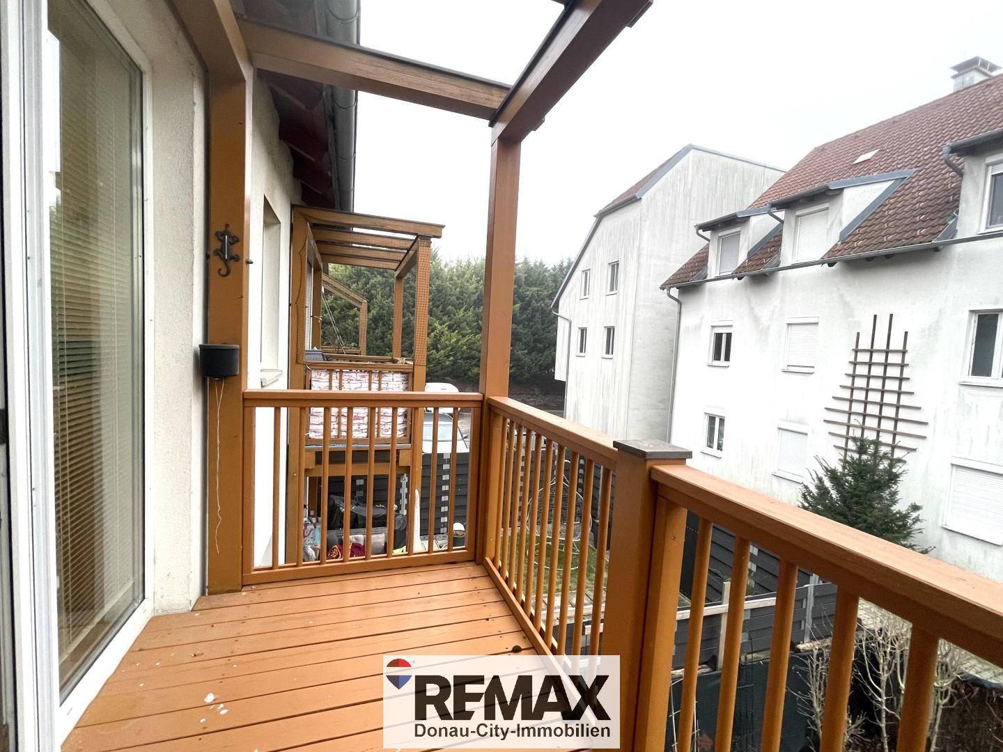 Überdachter Holzbalkon mit Blick auf die umliegenden Gebäude und Bäume.