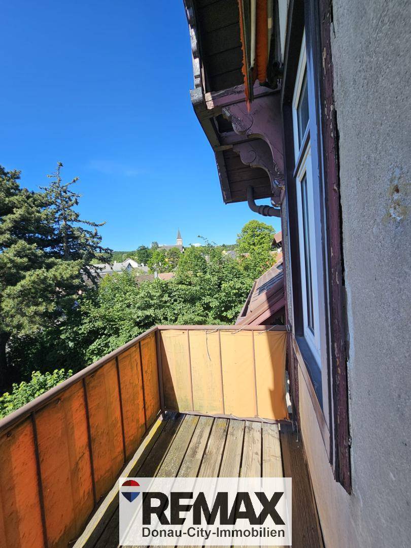 Kleiner, traditioneller Balkon mit Holzboden und Blick auf Bäume und die entfernte Stadt.