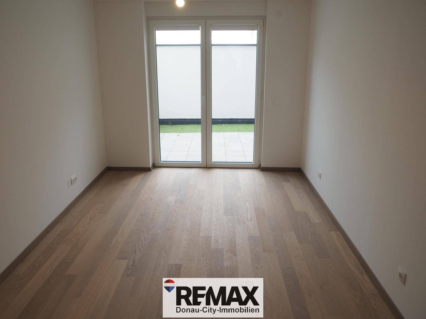Helles Zimmer mit Holzboden und großem Fenster zum Außenbereich.