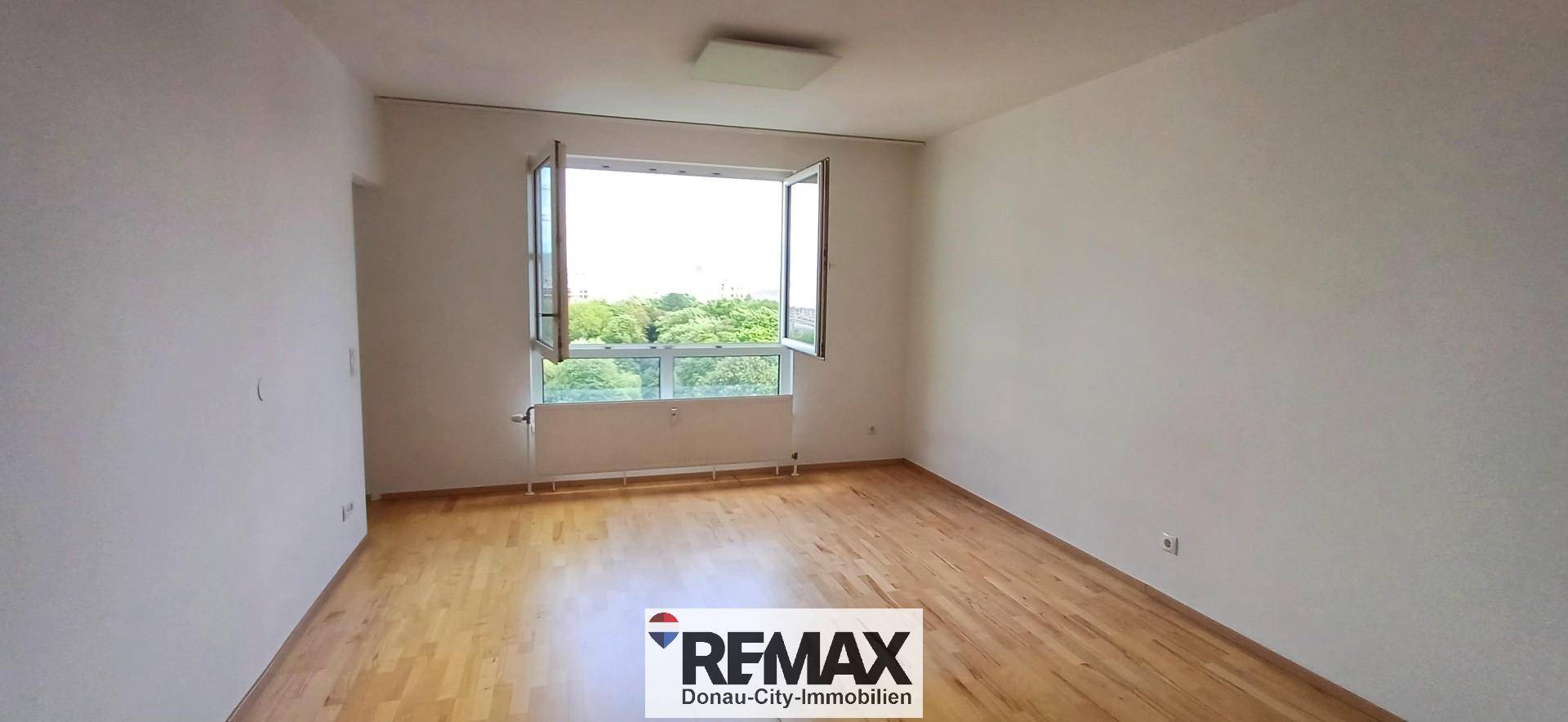 Leeres Zimmer mit hellem Holzfußboden und einem Fenster mit Blick ins Grüne.