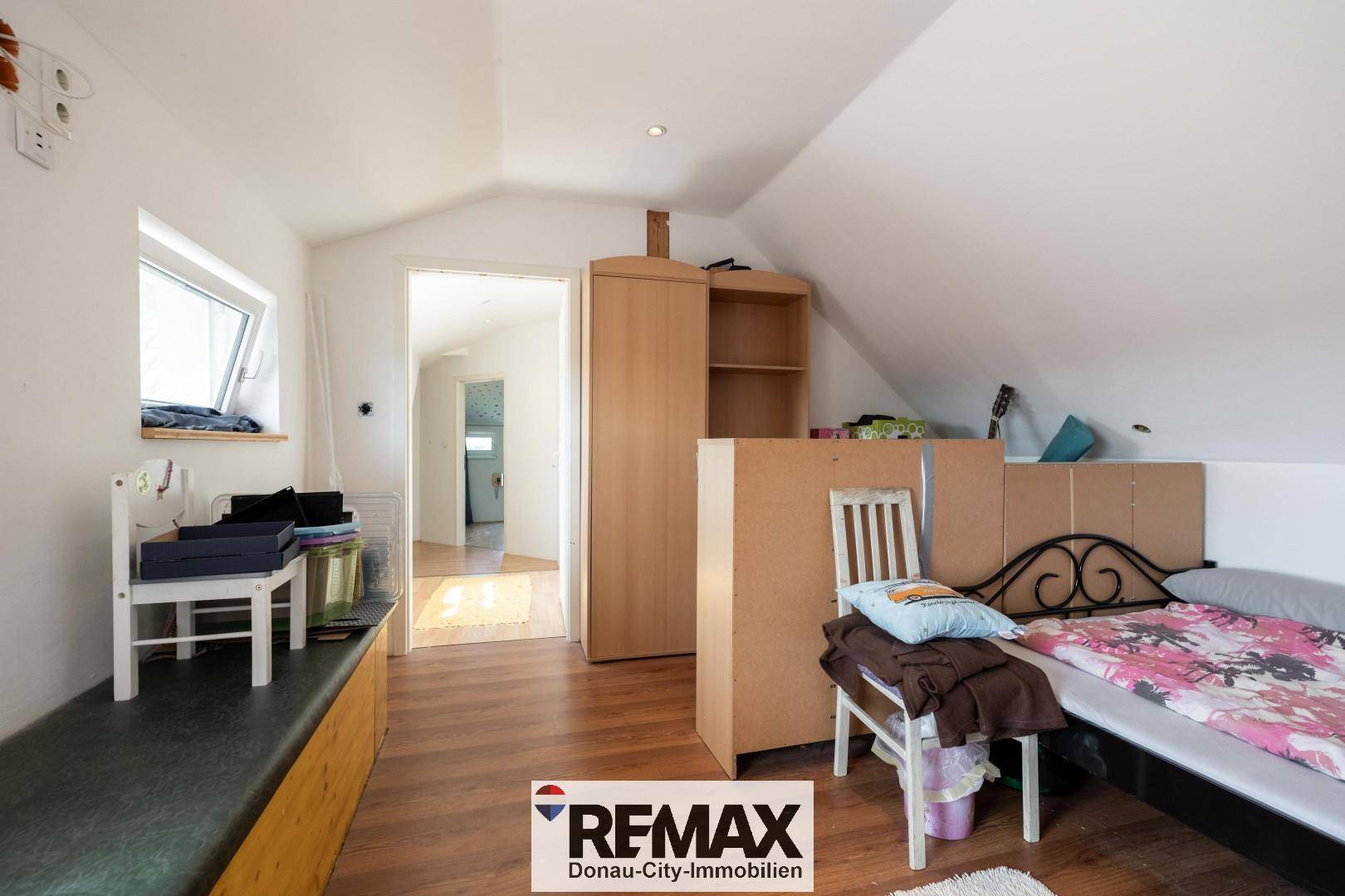 Helles Schlafzimmer im Dachgeschoss mit Einzelbett, Schrank und Fenster.