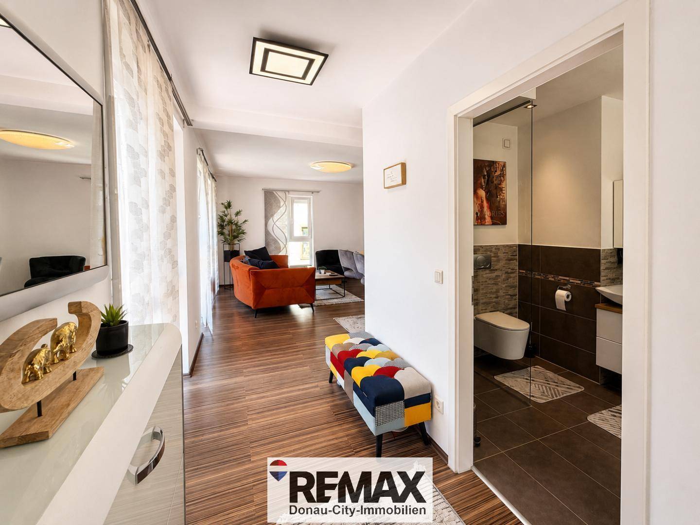 Geräumiger Flur mit Holzboden, farbenfroher Sitzbank und Zugang zum Badezimmer.