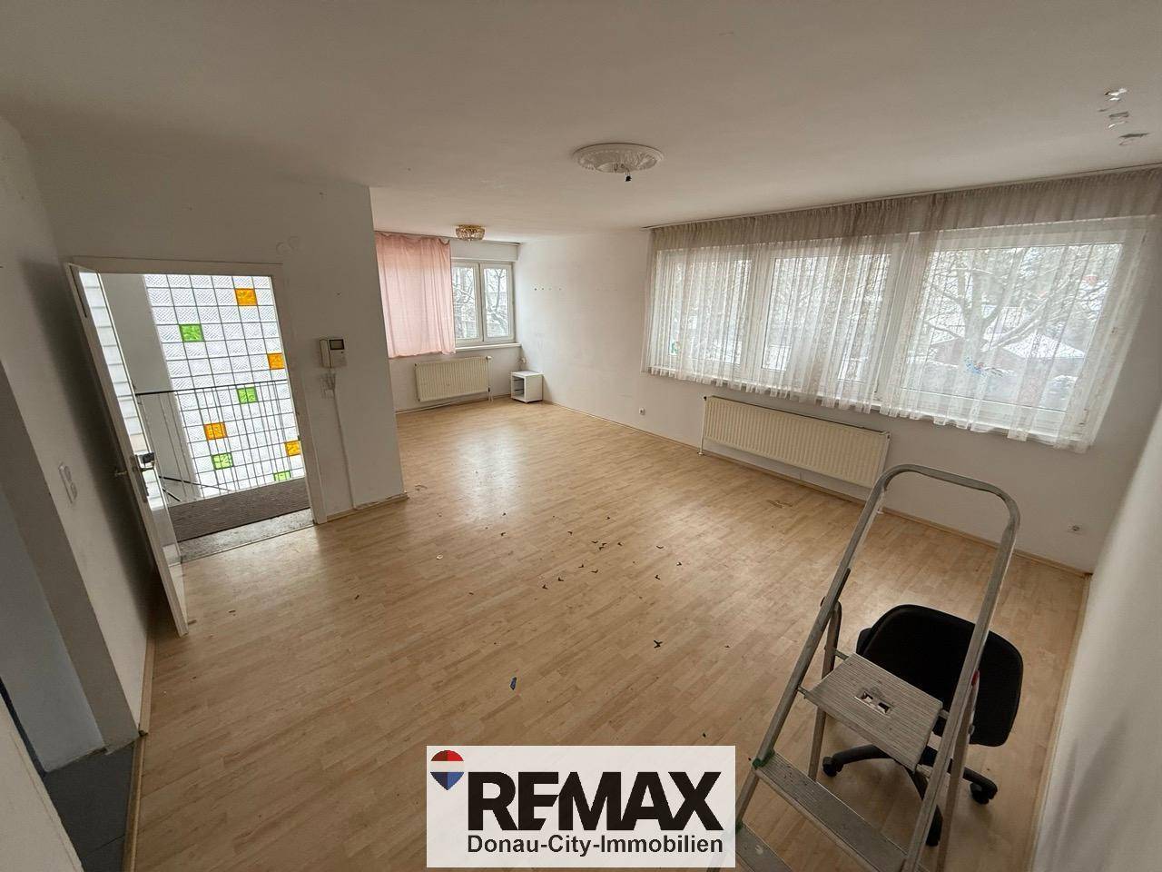 Großes Wohnzimmer mit Laminatboden und Fenstern, die den Raum mit Tageslicht füllen.