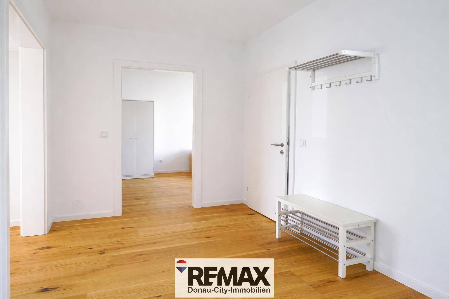 Heller Flur mit Holzboden, einfacher Garderobe und Schuhbank.