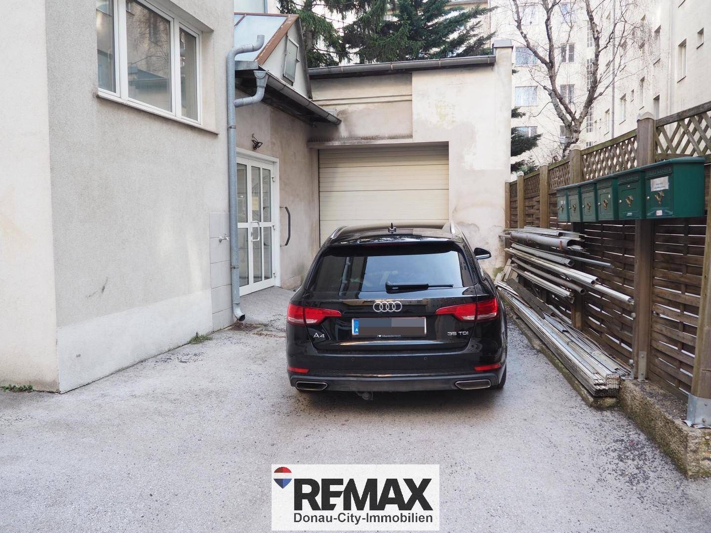 Rückseite eines Gebäudes mit einer Garage und einem geparkten Auto auf dem gepflasterten Hof.