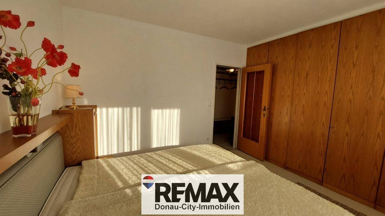 Helles Schlafzimmer mit Doppelbett, Holzschränken und Zugang zu einem begehbaren Kleiderschrank.
